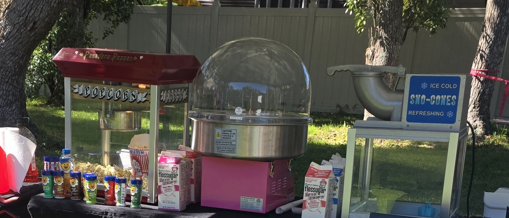 Popcorn, cotton candy and sno-cone machines set up on one concession table at an event